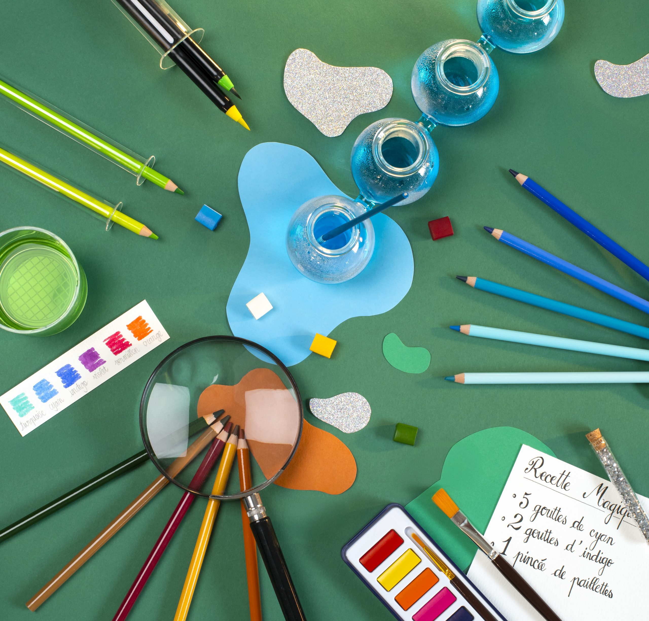 paints, paintbrushes, magnifying glasses and paper on bright green background
